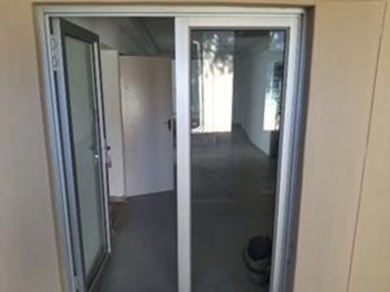 An empty office space featuring aluminium sliding doors and neutral tiled flooring, providing a clean and versatile work environment.