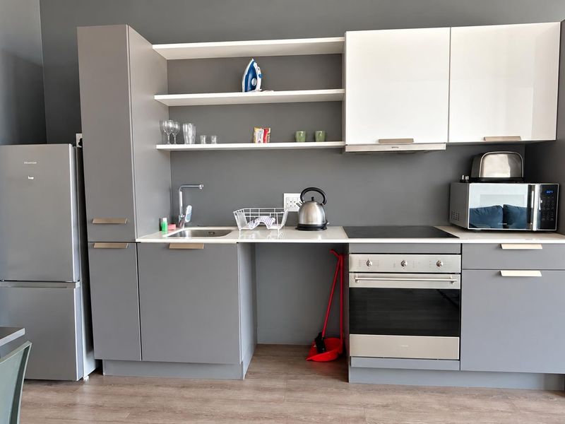 Modern kitchen featuring grey and white cabinetry, integrated appliances including an oven and hob, and open shelving for storage.