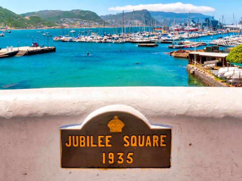 A scenic view overlooking the marina and harbor, featuring a historic Jubilee Square plaque mounted on a stone wall in the foreground.