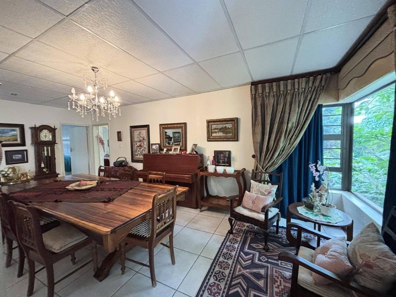 A traditional dining room featuring tiled flooring, a large window with garden views, and a classic crystal chandelier.