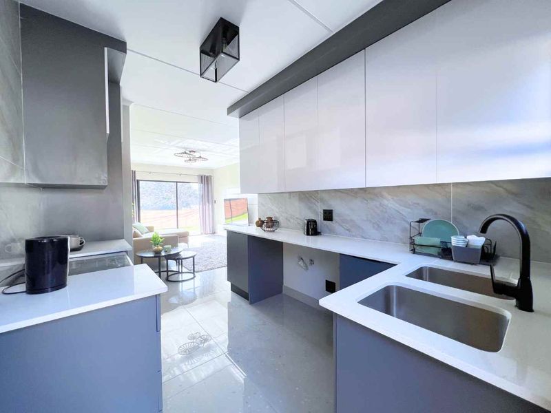 Modern open-plan kitchen featuring sleek glossy cabinetry, stone countertops, marble-look backsplash, and high-quality matte black fixtures, flowing into the adjacent living area.