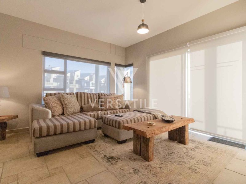 A bright and well-maintained living room featuring tiled flooring, modern pendant lighting, and large sliding glass doors with roller blinds.