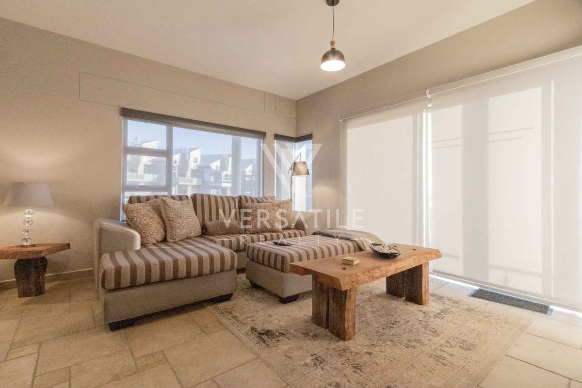 A bright and well-maintained living room featuring tiled flooring, modern pendant lighting, and large sliding glass doors with roller blinds.