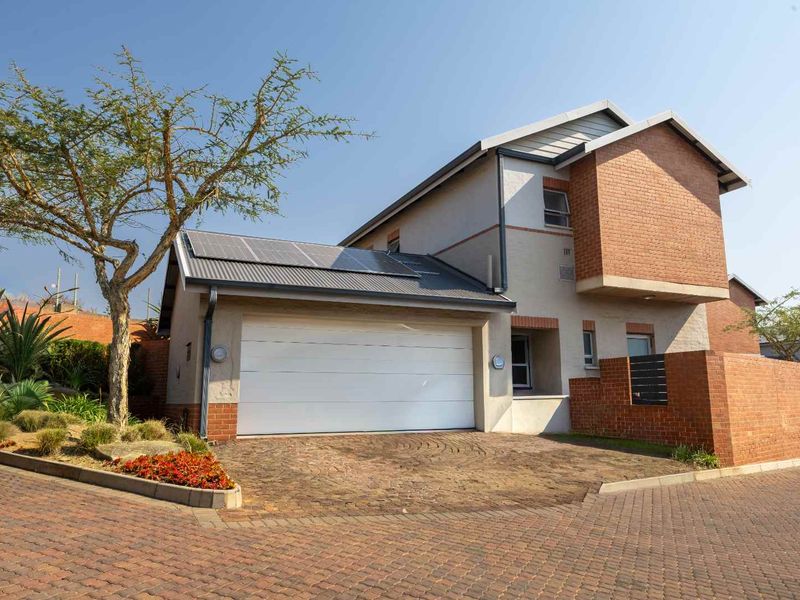 Front elevation of a modern townhouse featuring a double garage, brick and plaster facade, and roof-mounted solar panels.