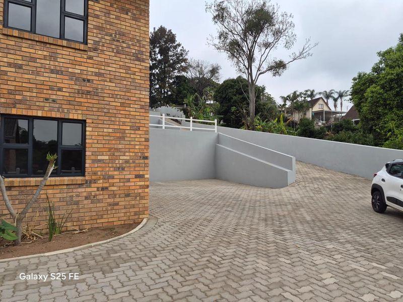 Exterior view of a townhouse featuring a face brick facade, paved driveway, and a modern grey retaining wall with white balustrading.