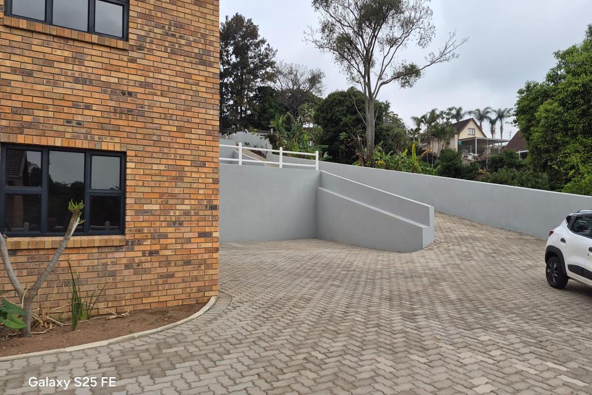 Exterior view of a townhouse featuring a face brick facade, paved driveway, and a modern grey retaining wall with white balustrading.