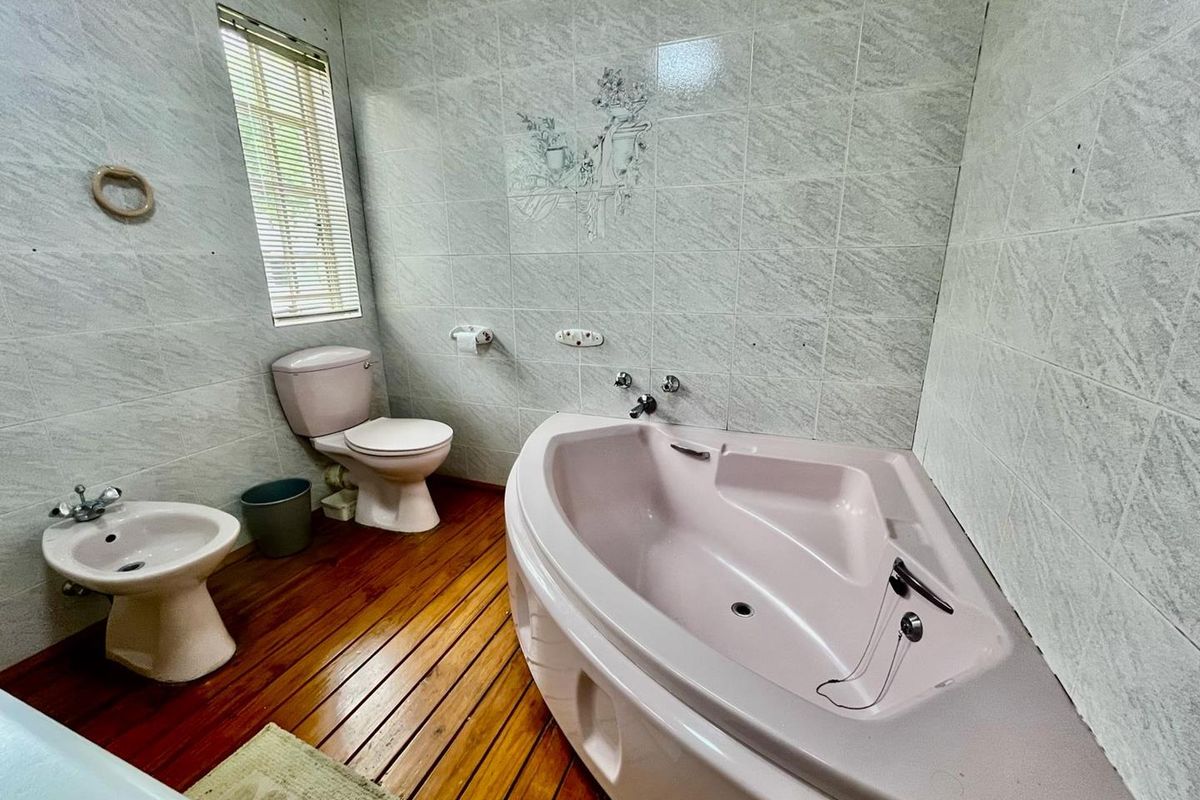 A dated bathroom featuring a corner bathtub, toilet, and bidet with tiled walls and timber flooring.