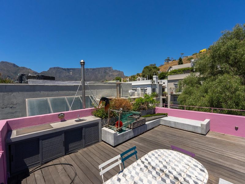 Spacious rooftop terrace featuring timber decking, a built-in concrete bench, and an outdoor kitchenette with sink, offering scenic mountain views.