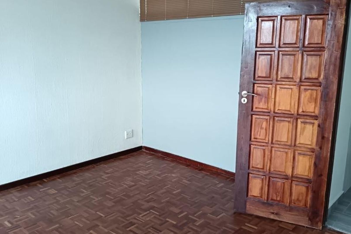 An empty bedroom featuring classic parquet flooring, a solid wooden panel door, and fitted venetian blinds.