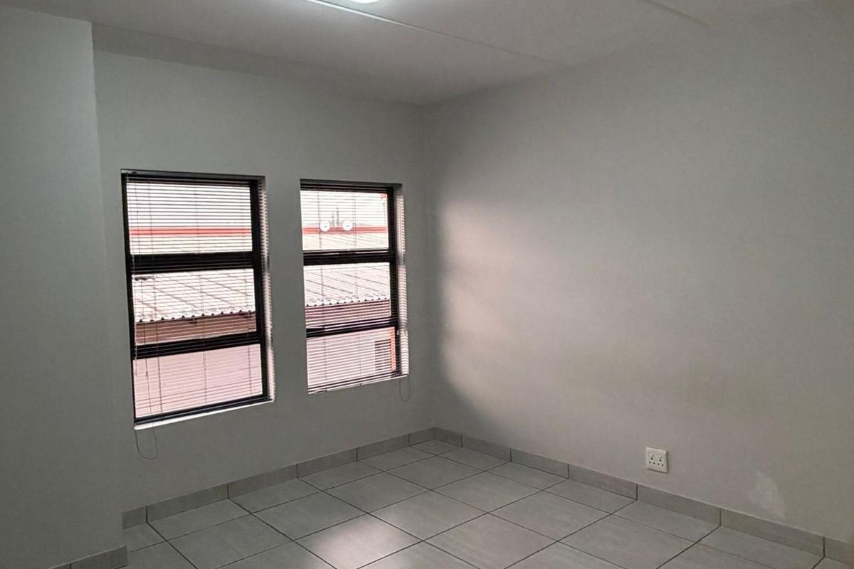 A bright, empty bedroom featuring neutral tiled flooring, clean walls, and dual windows fitted with horizontal blinds.