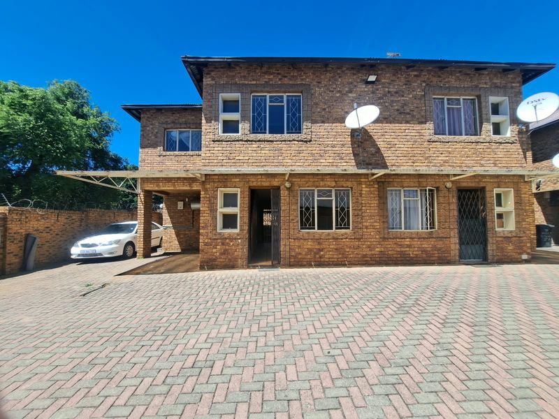 Front elevation of a double-story face brick townhouse featuring a paved driveway, integrated carport, and secure entrance.