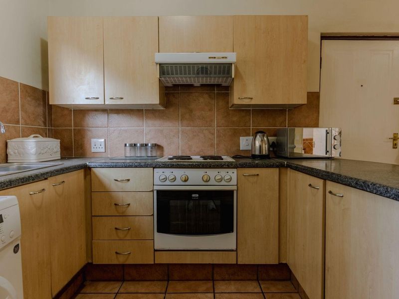 A functional kitchen featuring light wood-finish cabinetry, granite-look countertops, a built-in oven with hob, and a tiled backsplash.