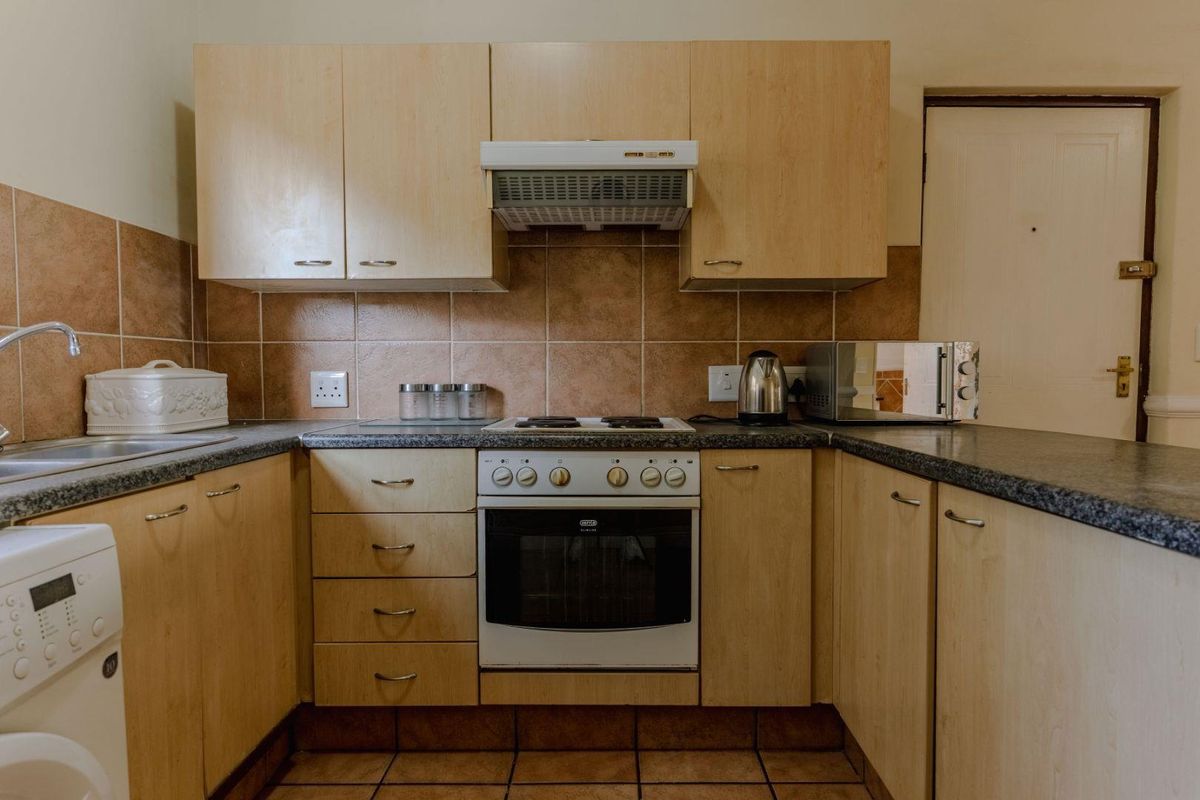 A functional kitchen featuring light wood-finish cabinetry, granite-look countertops, a built-in oven with hob, and a tiled backsplash.