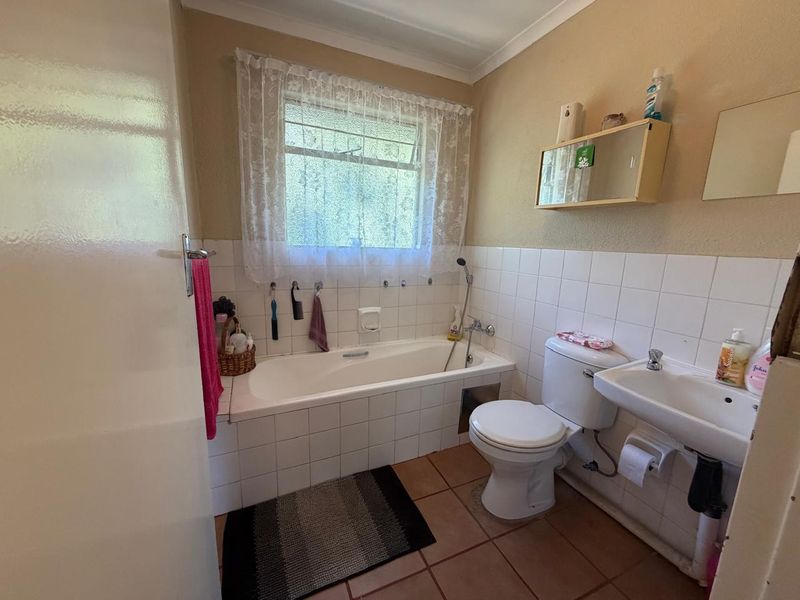 A dated bathroom featuring a built-in bathtub, pedestal washbasin, and toilet, with ceramic tiling throughout. The space would benefit from modern updates.