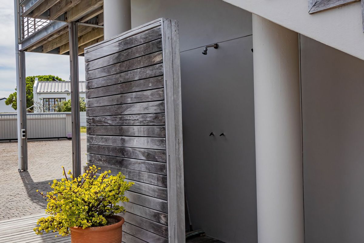 An outdoor shower area featuring a timber privacy screen, concrete columns, and timber decking, situated in a paved rear exterior space.