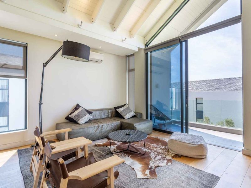 Bright living room featuring vaulted ceilings with exposed beams, timber flooring, and large sliding glass doors opening onto a private balcony.