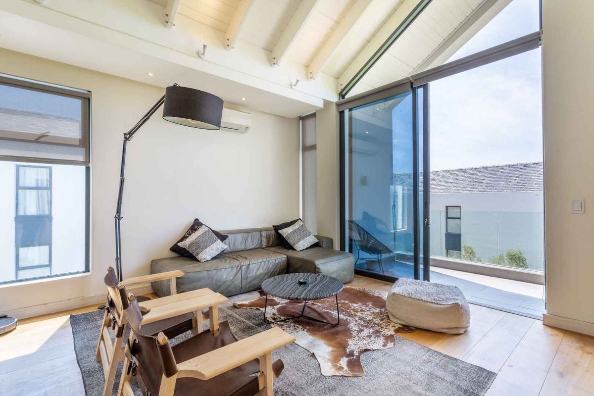 Bright living room featuring vaulted ceilings with exposed beams, timber flooring, and large sliding glass doors opening onto a private balcony.
