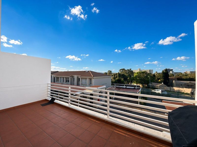 An open balcony featuring tiled flooring and a white metal balustrade, offering elevated views of the surrounding residential complex.