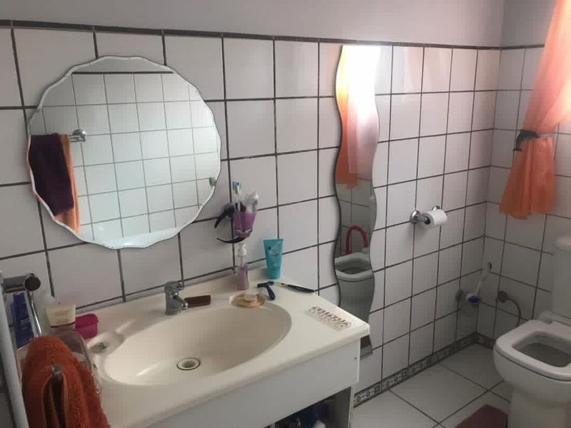 A functional bathroom featuring white wall and floor tiles, a vanity basin with mixer tap, and a standard toilet.
