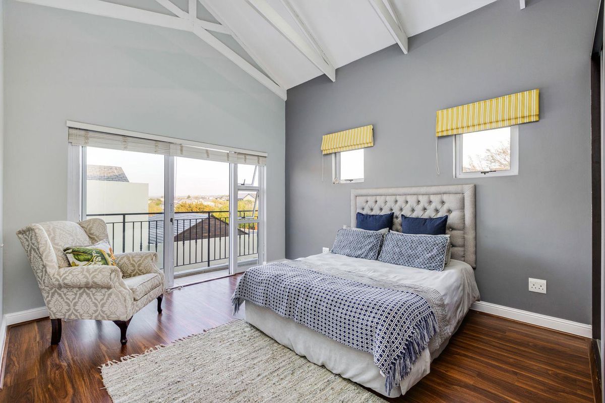 Spacious bedroom featuring high vaulted ceilings, dark wood-look flooring, and large sliding glass doors opening onto a private balcony with scenic views.
