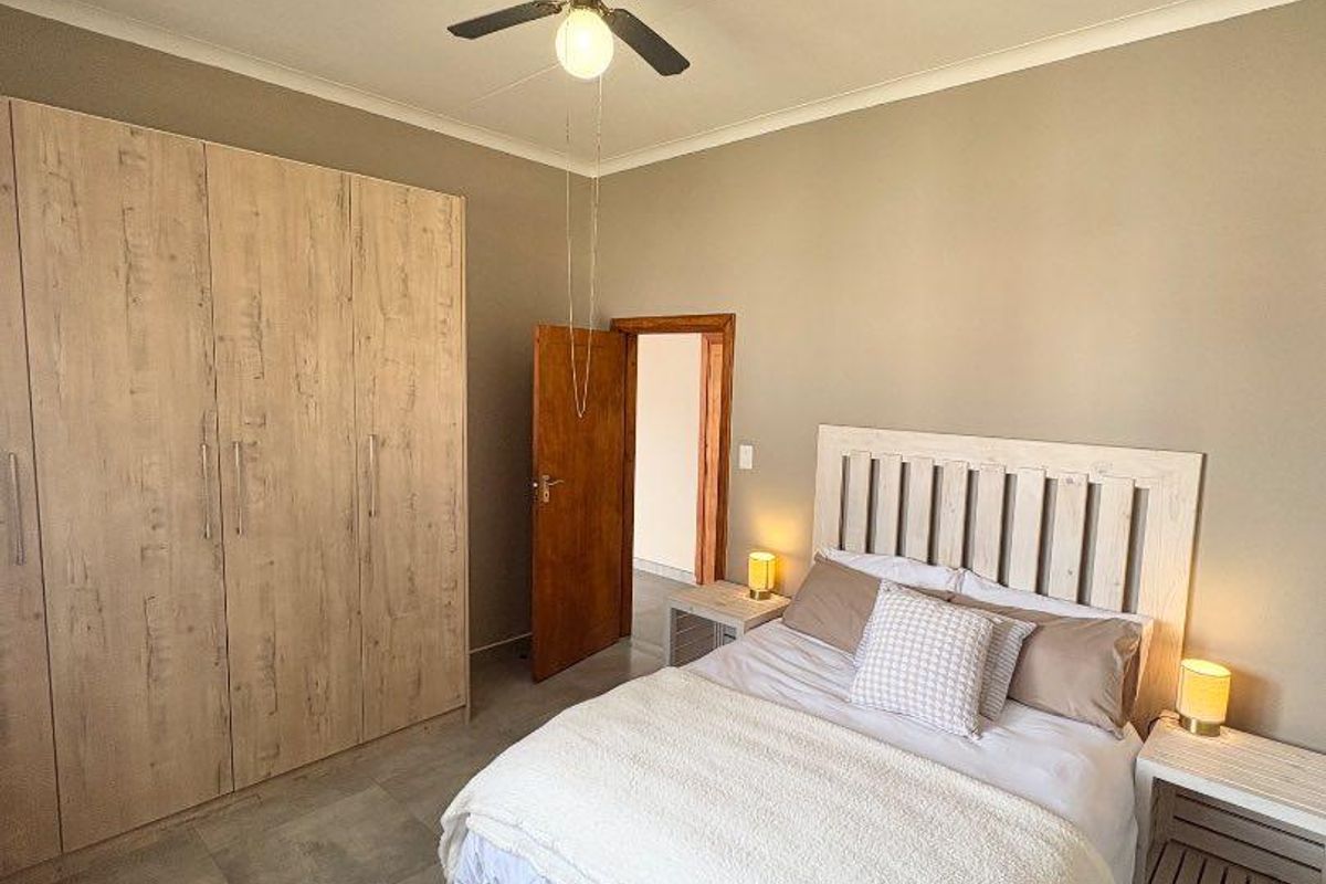A well-maintained bedroom featuring built-in wooden cupboards, tiled flooring, and a ceiling fan.