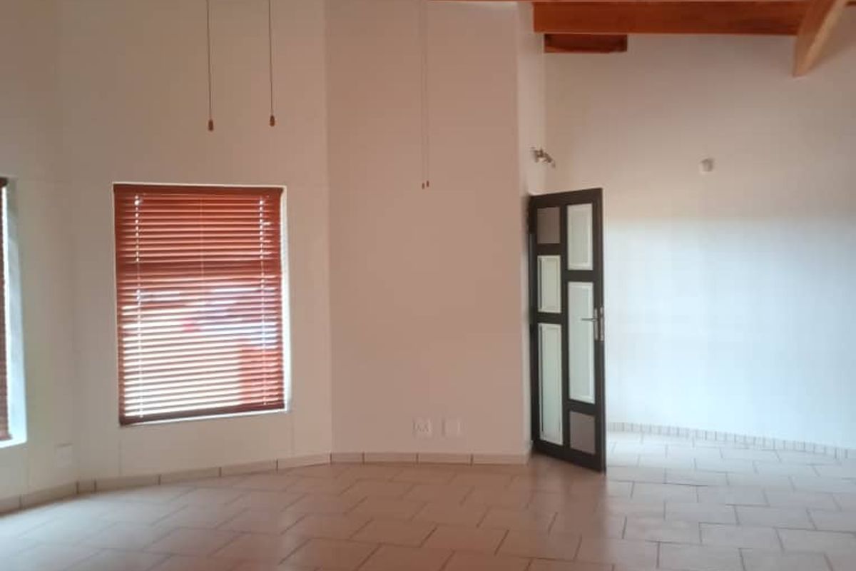 Spacious living area featuring high vaulted timber ceilings with exposed beams, tiled flooring, and a modern dark-framed glass door.