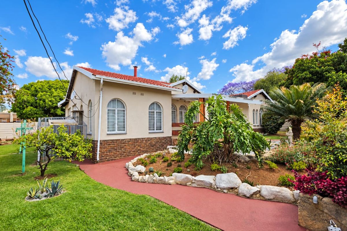 A well-maintained rear exterior view of the house featuring a terracotta tiled roof, arched windows with security bars, and a landscaped garden with paved pathways.