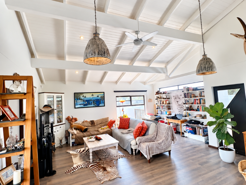 Spacious living room featuring a high vaulted ceiling with exposed beams, pendant lighting, ceiling fan, and built-in shelving units.