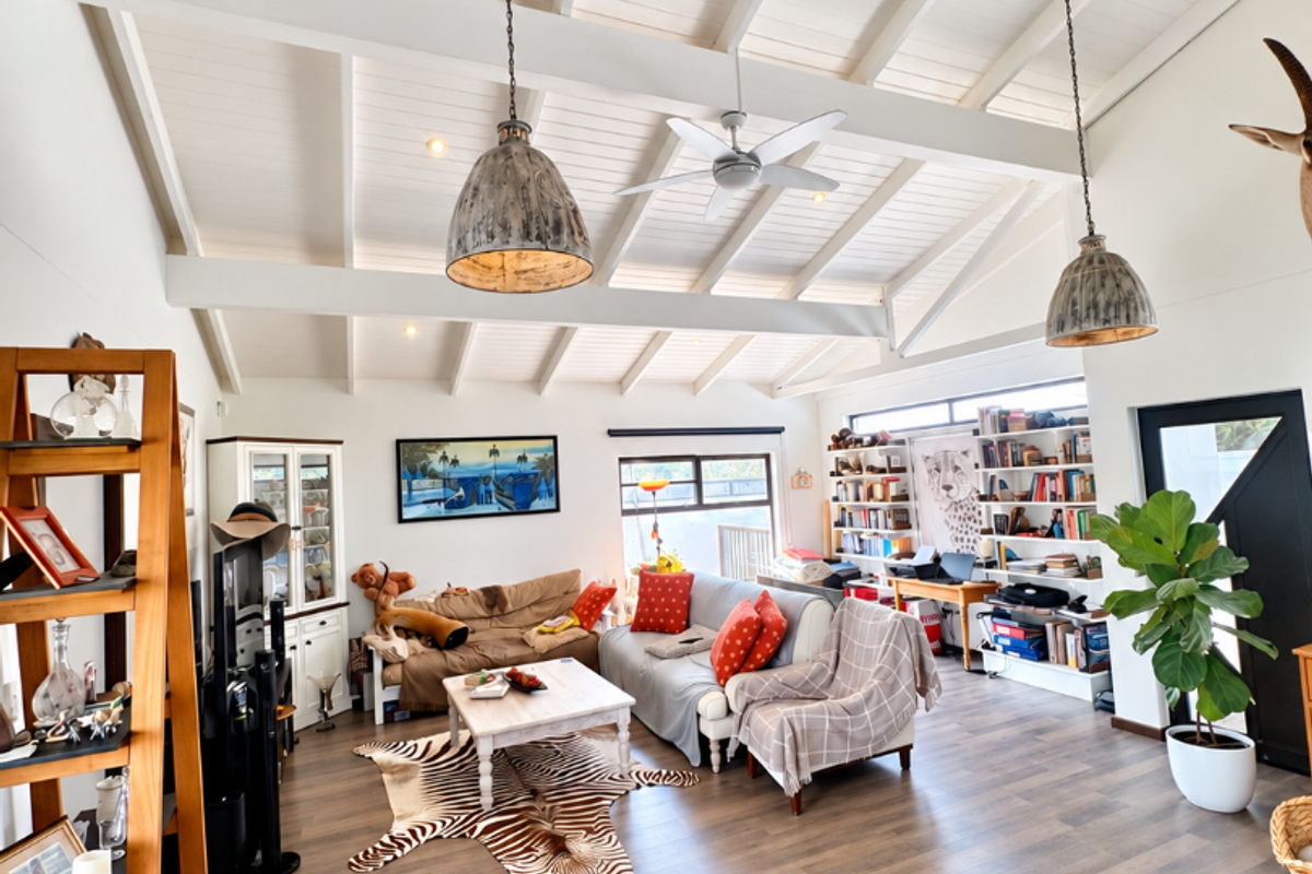 Spacious living room featuring a high vaulted ceiling with exposed beams, pendant lighting, ceiling fan, and built-in shelving units.