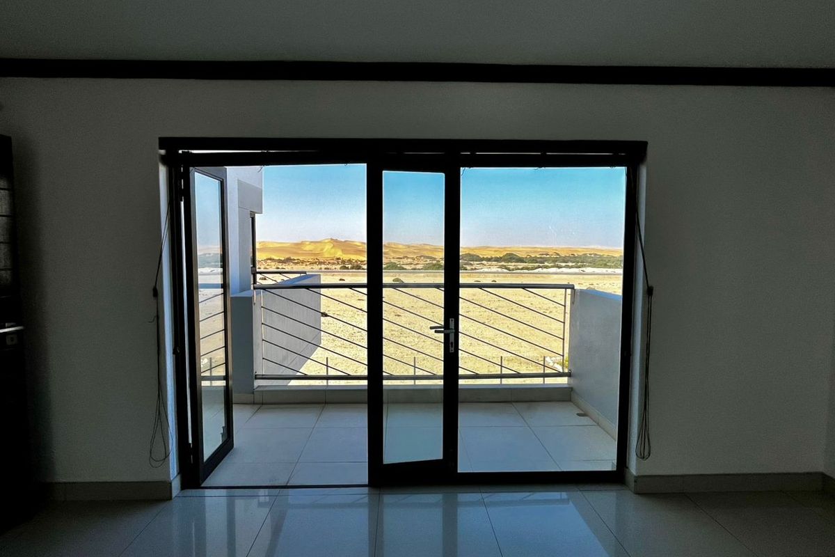 Interior view looking out through large glass sliding doors onto a private balcony with scenic desert landscape views.