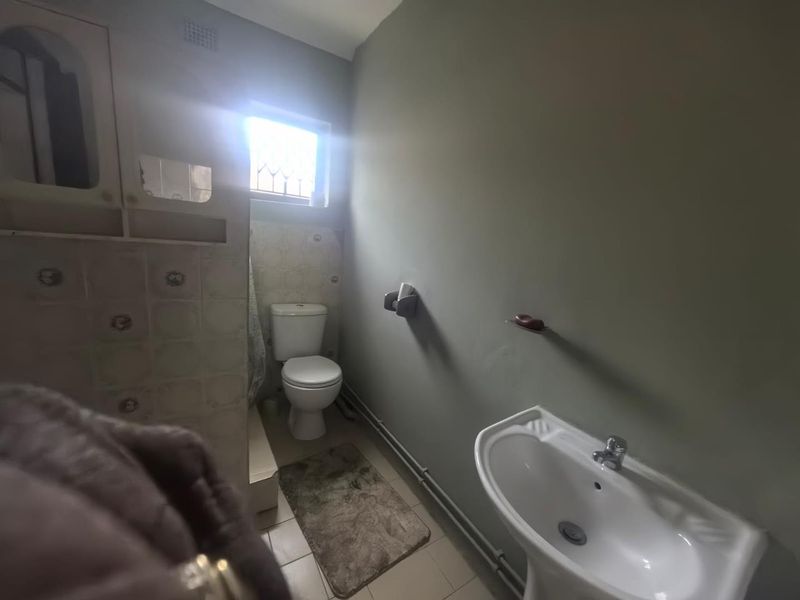 A functional bathroom featuring a pedestal washbasin, toilet, and tiled splashback, requiring cosmetic updates to modernize the space.