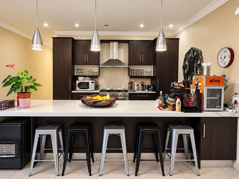 Modern kitchen featuring dark wood cabinetry, a large central island with stone countertop, stainless steel appliances, and contemporary pendant lighting.