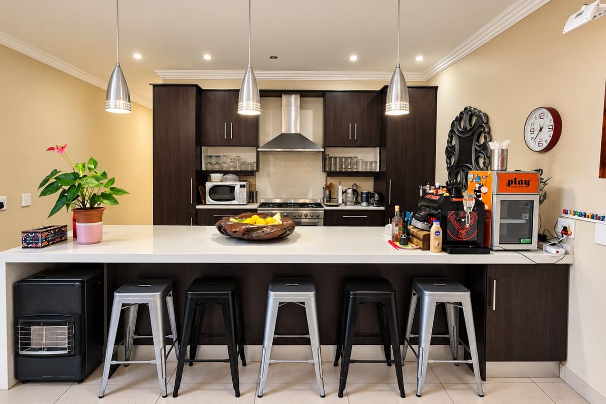 Modern kitchen featuring dark wood cabinetry, a large central island with stone countertop, stainless steel appliances, and contemporary pendant lighting.
