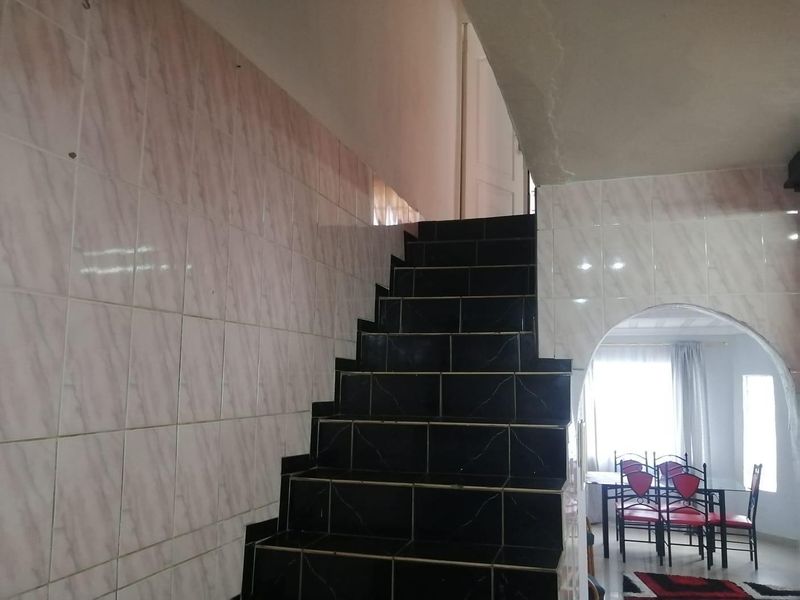 A hallway featuring a tiled staircase and wall cladding with an arched opening leading to an adjacent living area.