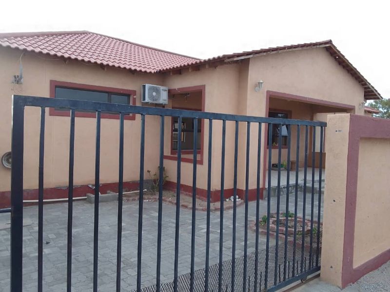 Front view of a single-story house featuring a paved driveway, metal security gate, and covered entrance area with an installed air conditioning unit.