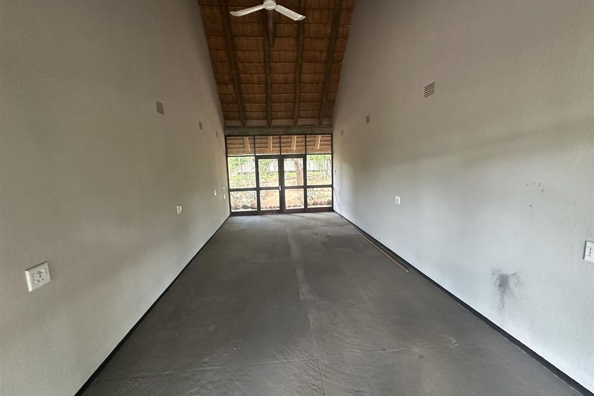 An empty, unfinished interior space featuring a high vaulted thatched ceiling, exposed concrete flooring, and large glass panel doors leading to the exterior.
