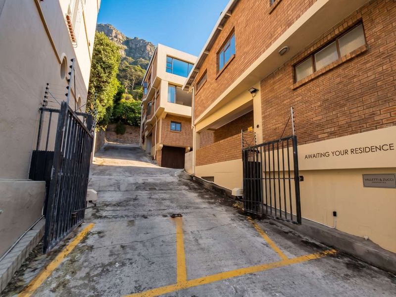 Exterior view of the apartment complex entrance featuring a concrete driveway, brick facade, and secure metal gate with electric fencing.