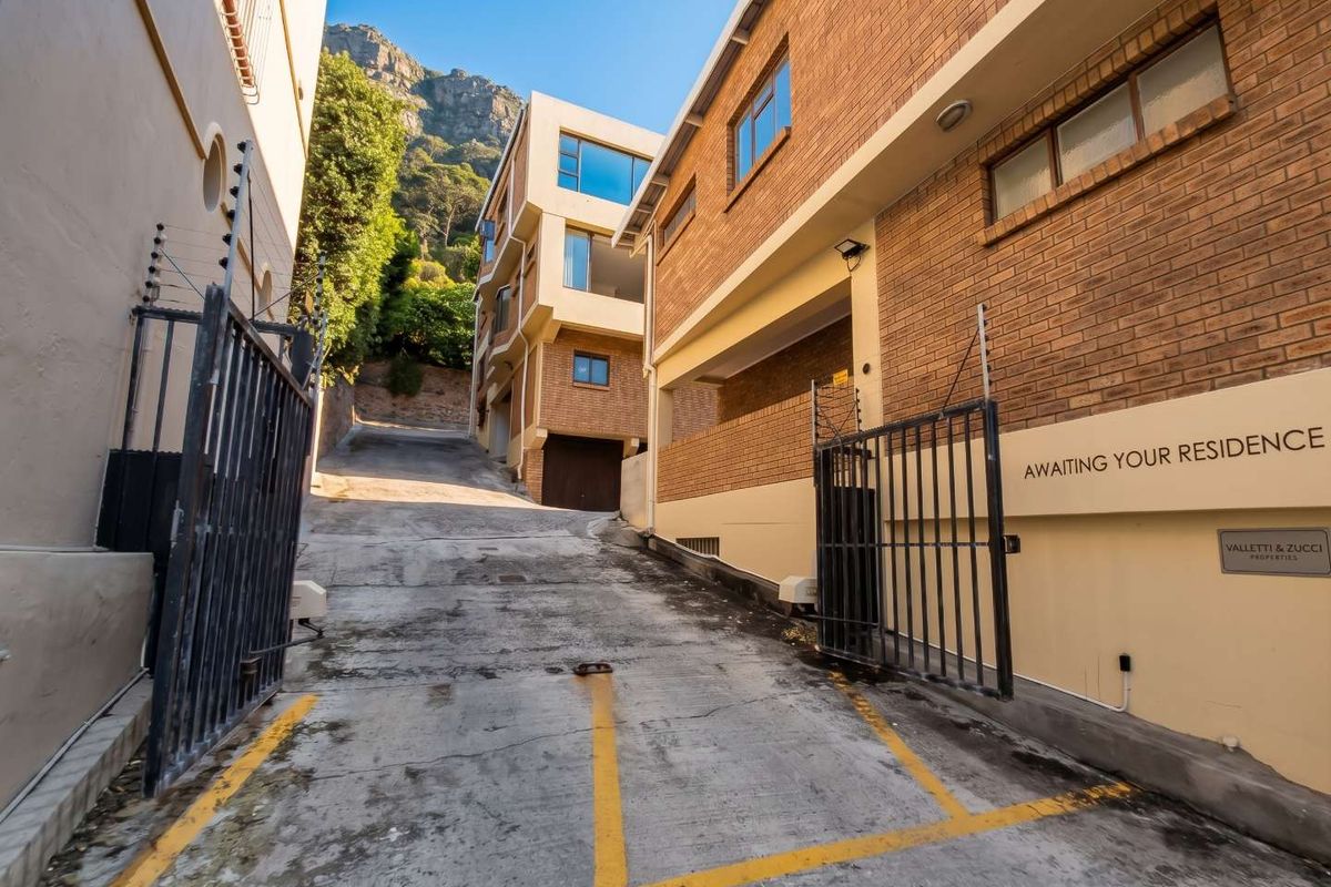 Exterior view of the apartment complex entrance featuring a concrete driveway, brick facade, and secure metal gate with electric fencing.