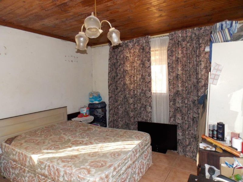 A bedroom featuring a timber ceiling and tiled flooring, currently requiring cosmetic updates and wall repairs to improve its overall condition.