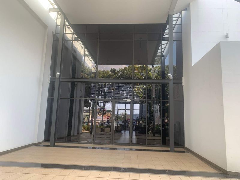 A spacious and modern office building entrance featuring a large glass facade, metal framing, and clean tiled flooring.