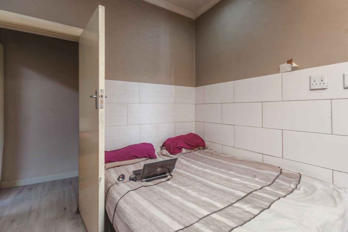 A compact bedroom featuring partial wall tiling and laminate flooring, currently utilized as a sleeping and workspace area.