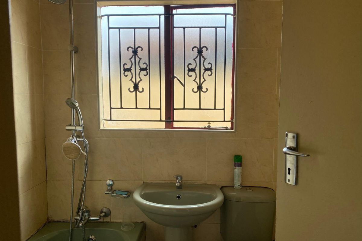 A compact bathroom featuring a pedestal basin, toilet, and a shower-over-bath combination with security bars on the window.