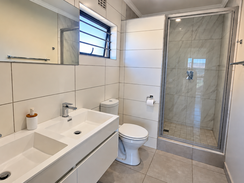 Modern bathroom featuring a double vanity, glass-enclosed shower, and neutral tiled finishes throughout.