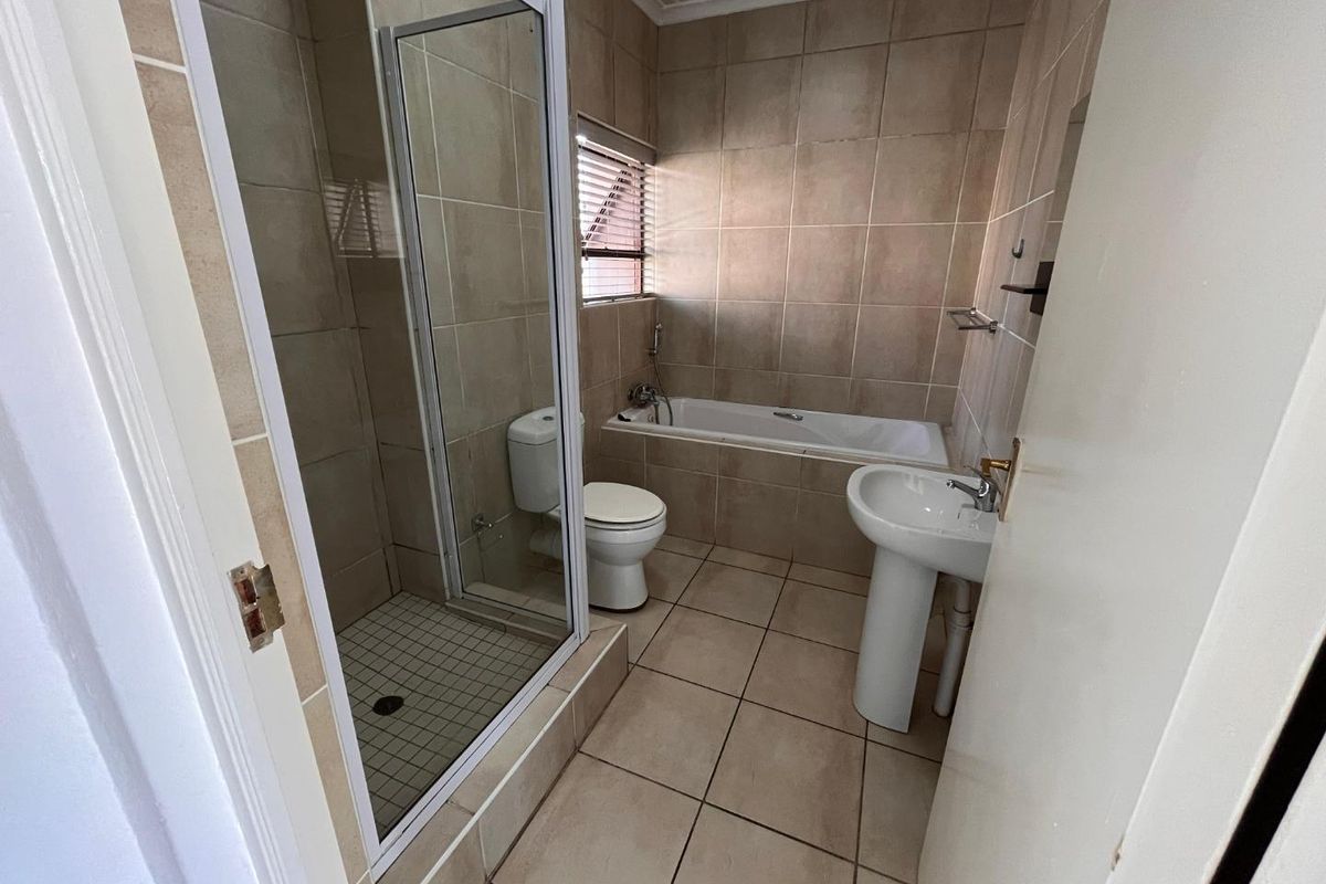 A functional bathroom featuring a separate shower enclosure, a bathtub, a pedestal basin, and neutral floor-to-ceiling wall tiling.