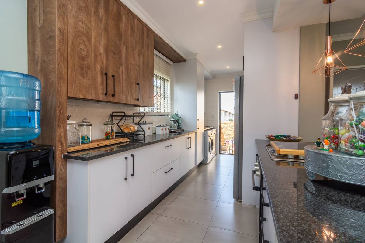 Modern galley-style kitchen featuring wood-grain upper cabinetry, white lower cabinets, granite countertops, and integrated laundry area with direct outdoor access.