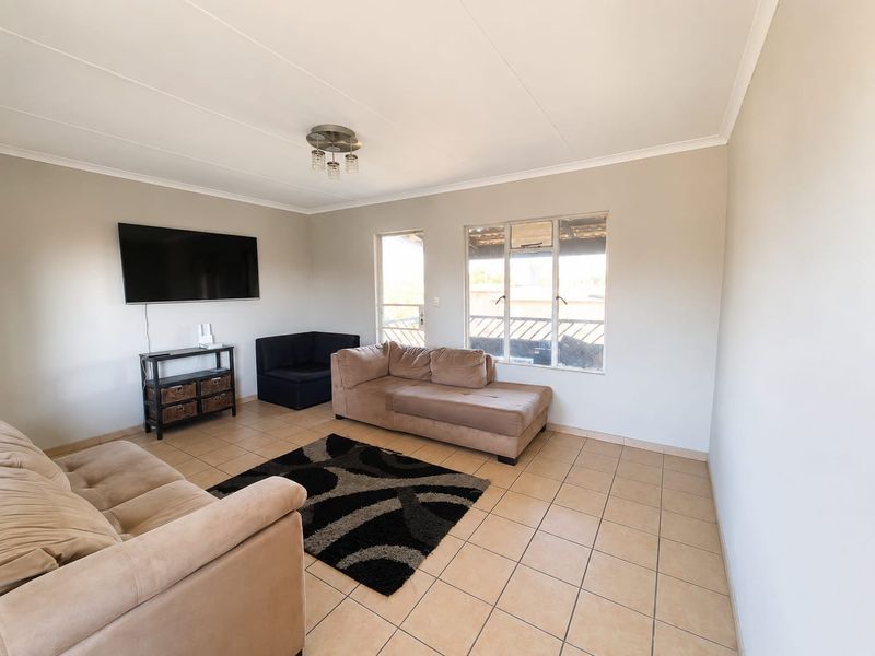 A bright living room featuring neutral wall tones, tiled flooring, and large windows providing natural light.