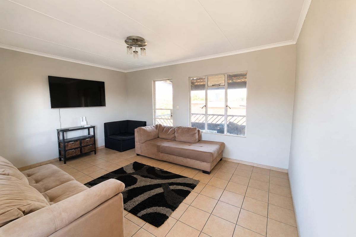 A bright living room featuring neutral wall tones, tiled flooring, and large windows providing natural light.