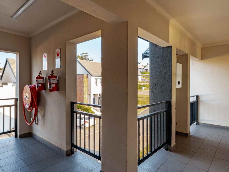 A clean, well-maintained apartment complex hallway featuring tiled flooring, metal safety railings, and essential fire safety equipment.