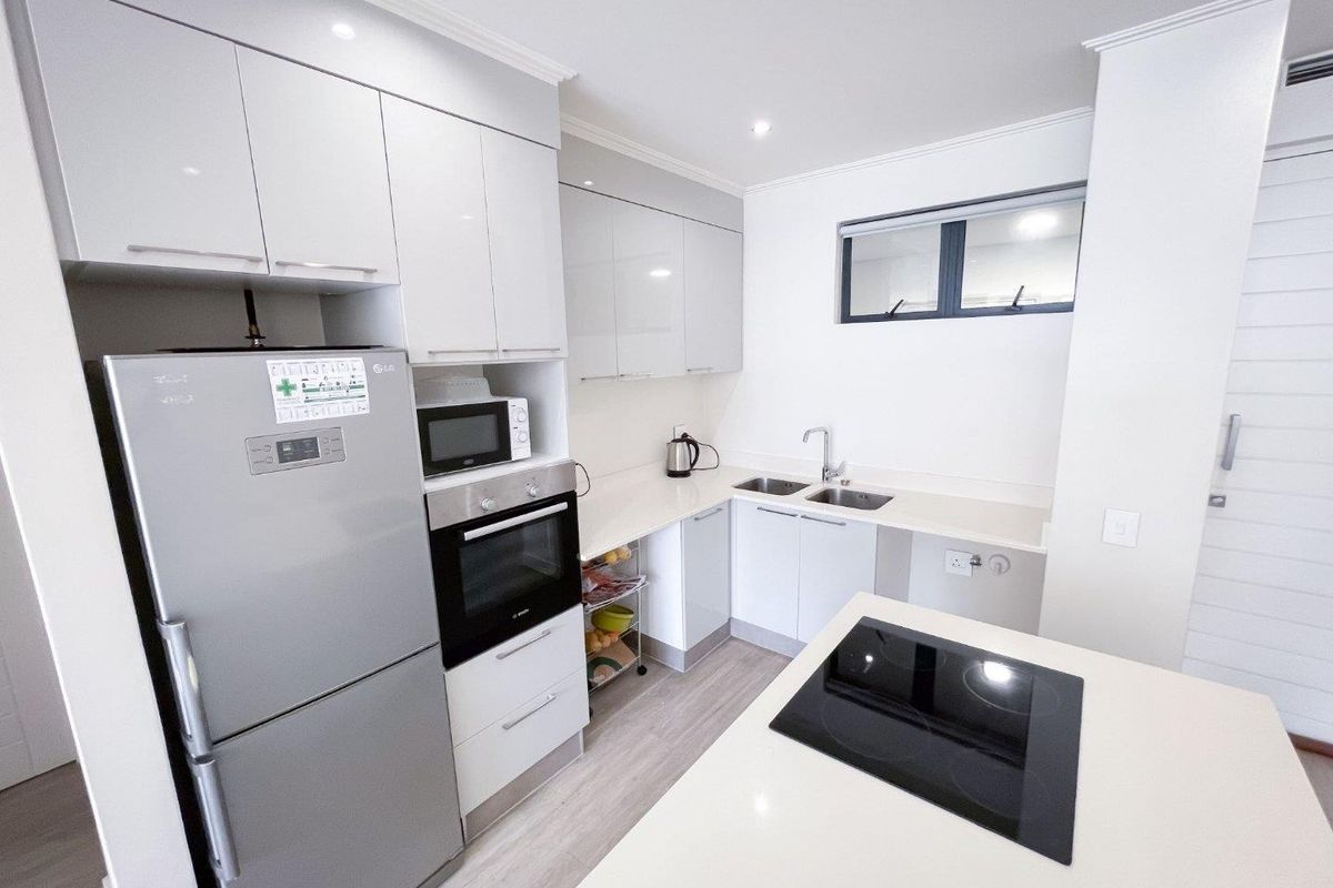 Modern kitchen featuring sleek white cabinetry, stone countertops, a double sink, and a central island with an integrated electric hob.