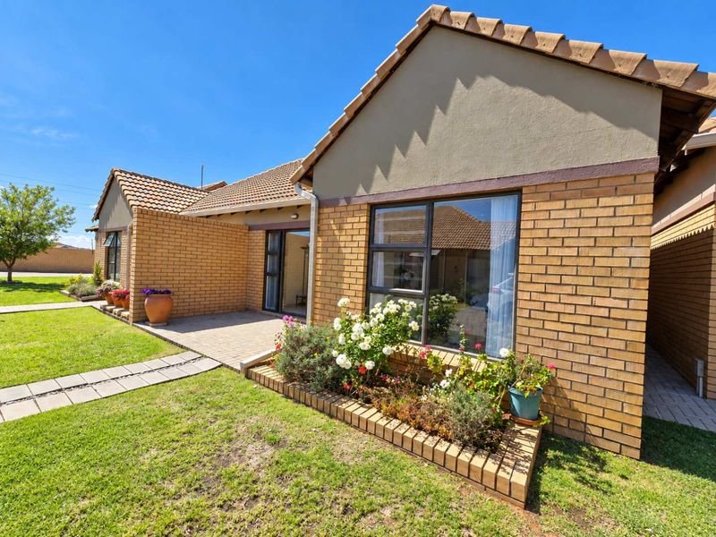 A well-maintained rear exterior view featuring a brick facade, tiled roof, paved patio area, and a landscaped brick garden bed.